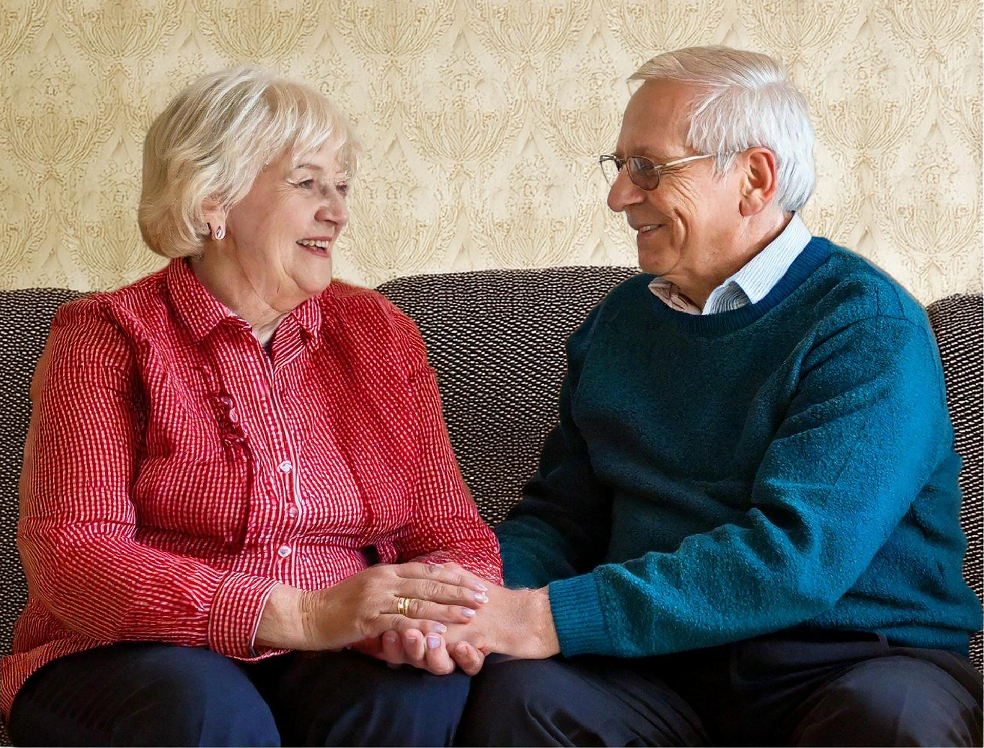 Couple de personnes âgées se tenant la main sur un canapé à domicile, illustrant la promesse de L'Essentiel : ne pas séparer les couples grâce au lit médicalisé double.